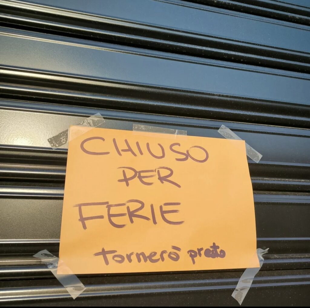 Handwritten holiday closure sign on a shop shutter in Rome