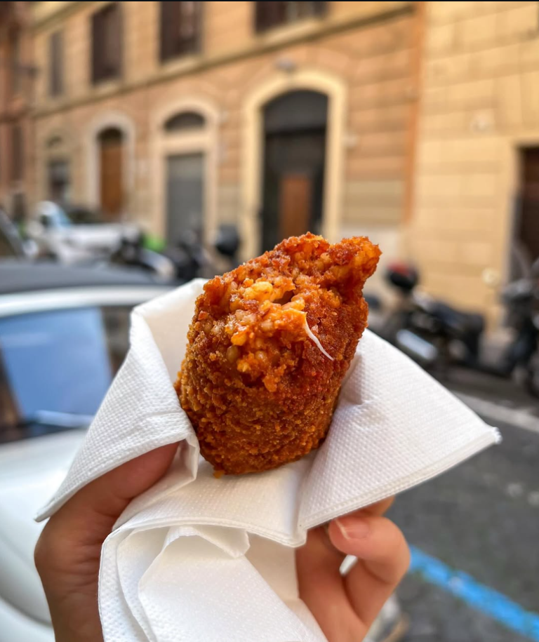Supplì broken open in hand with a Rome street in the background