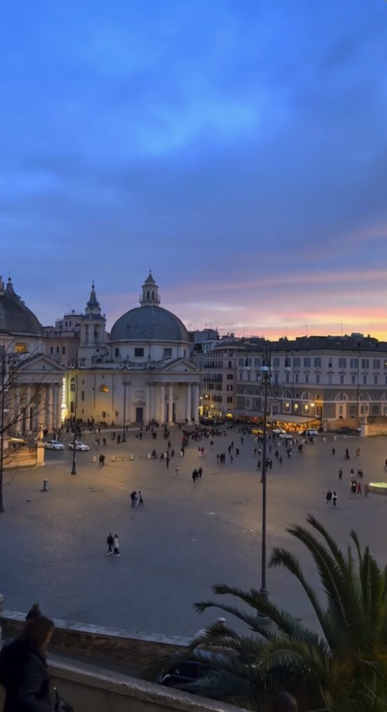 People walking through Piazza del Popolo at sunset